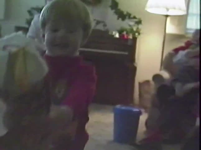 Vintage footage shows a happy toddler receiving a Christmas stocking from his family during a holiday gathering in the living room