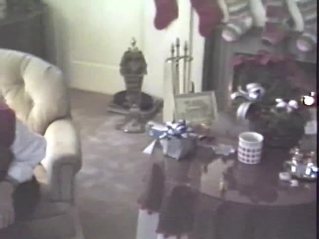 Vintage home video captures an elderly man opening a present and a woman talking during a Christmas celebration at home