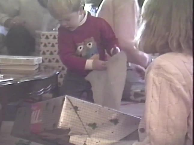 Vintage VHS footage shows a toddler excitedly opening presents with his family on Christmas morning