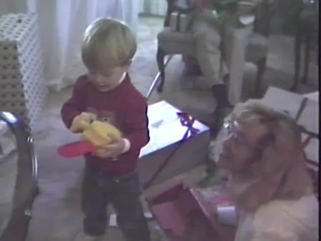 A young boy smiles as he plays with his new toy chainsaw on Christmas morning in this vintage home video