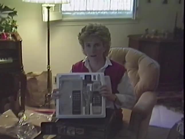 A woman happily opens a brand new set of silverware as a gift in a cozy living room, as captured on vintage VHS tape