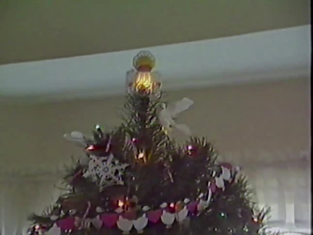 A slow pan up a Christmas tree, landing on a close-up of the lit-up angel tree topper, from a vintage home video