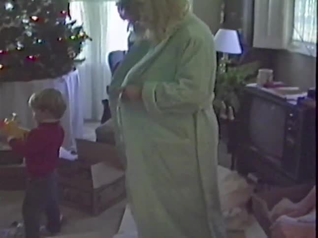 Vintage home video captures a mom happily trying on her new bathrobe on Christmas morning as her children play with toys