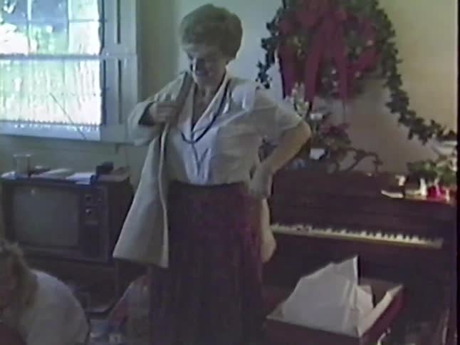 A woman happily opens a Christmas gift and tries on a new coat in a vintage 1980s home video