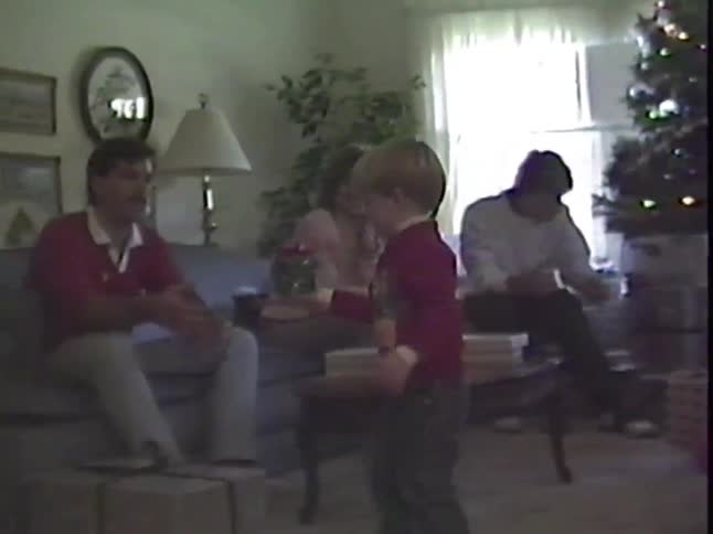Vintage home video of a young boy showing his family a Christmas gift in their living room