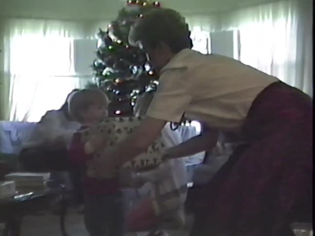 A family gathers in the living room to exchange gifts on Christmas morning in a nostalgic home video from the 1980s