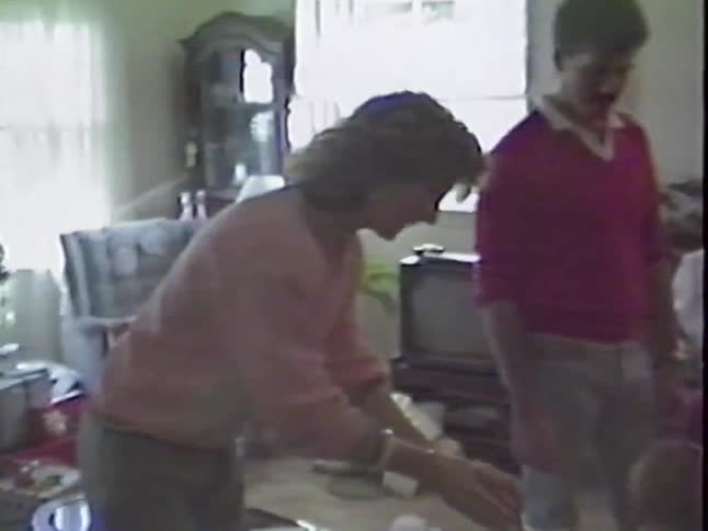 A young boy proudly shows off his new Christmas stocking to his family in a vintage home video from the 1980s
