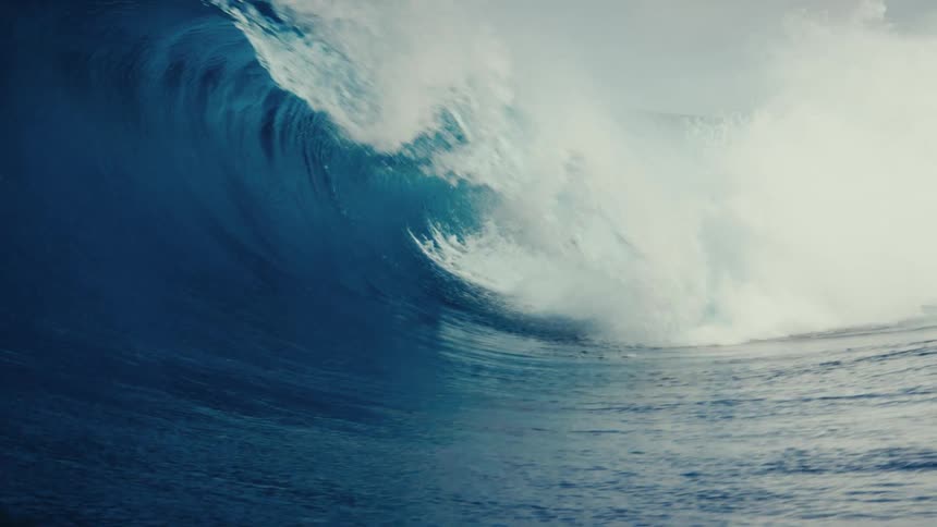 An epic slow-motion shot captures a massive, powerful blue ocean wave as it curls and breaks