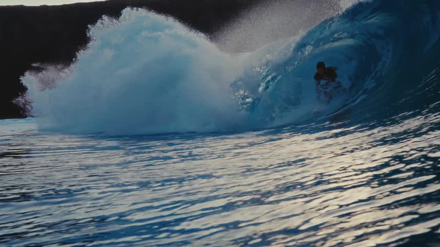 Epic slow motion view of a surfer carving through the barrel of a perfect blue wave at golden hour