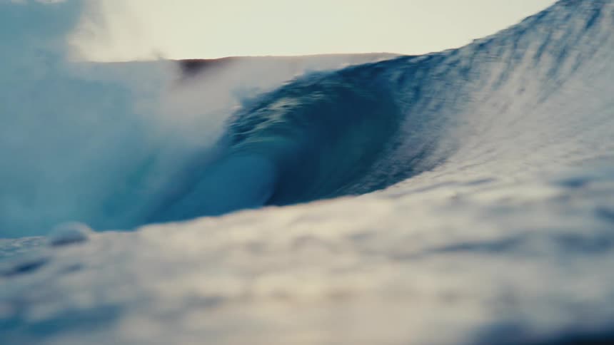 A beautiful blue ocean wave barrels and crashes in slow motion, with the camera being pulled under the water's surface