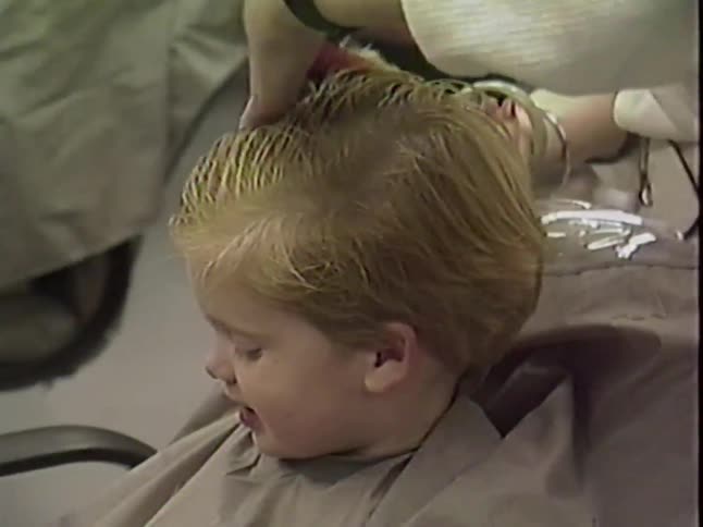 Vintage footage shows a close-up of a young blonde child getting a haircut in a salon chair