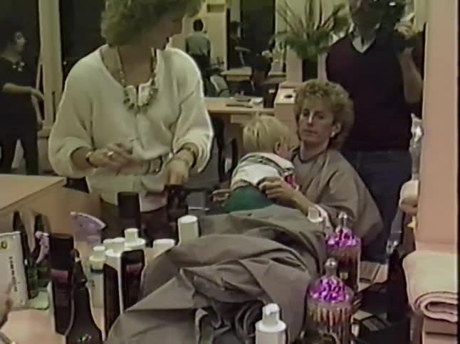 Vintage footage from the 1980s shows a baby boy getting his first haircut in a salon while sitting on his mother's lap