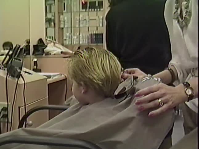 Vintage 1980s footage of a cute toddler sitting patiently while a stylist gives him a haircut in a salon