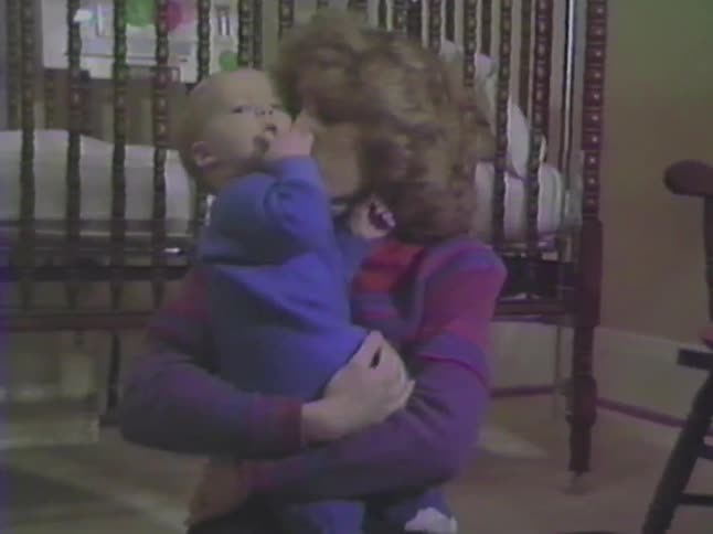 A loving mother holds and kisses her baby boy in his nursery in this sweet vintage home video