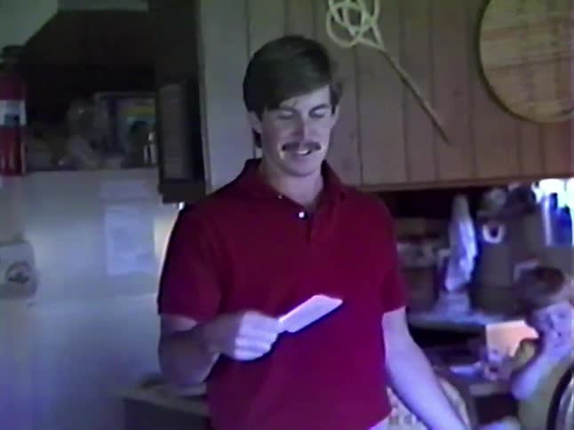 Vintage 1980s VHS footage captures a man with a mustache laughing and joking around in his kitchen at home