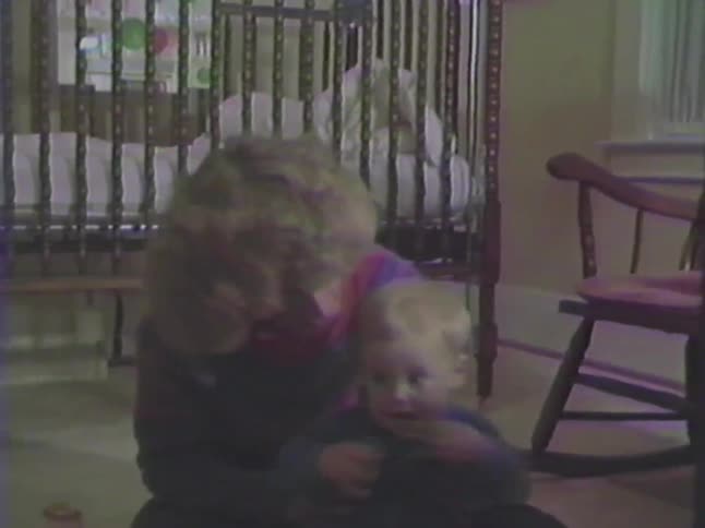 A proud mother holds her excited baby boy as he learns to wave in a sweet vintage home video
