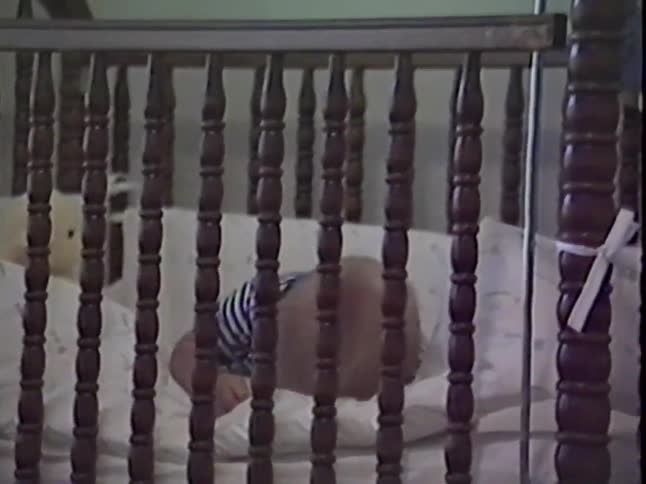 A baby slowly stands up in its crib in this authentic home video from 1987