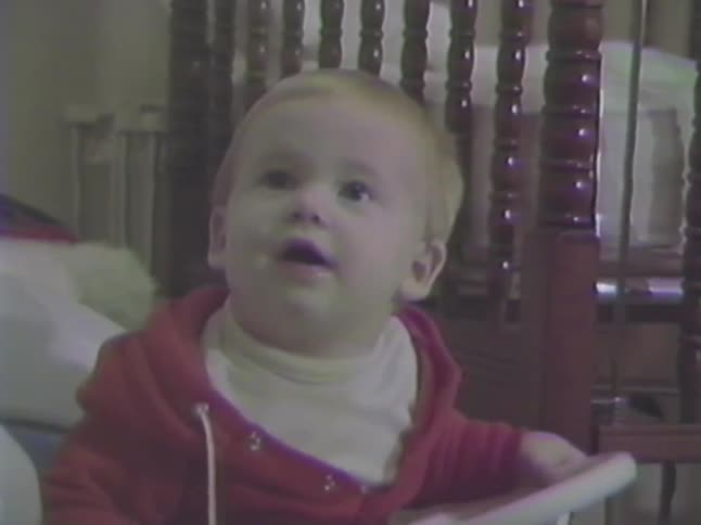 Vintage VHS home movie footage shows a cute baby in a red hoodie sitting in a toy car