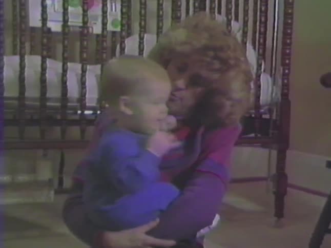 A mother holds and cuddles her baby boy in his nursery in a sweet vintage home video from the 1980s