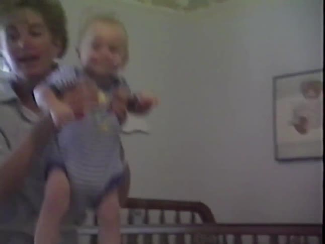 A mother lifts her happy baby boy out of his crib and helps him learn to walk with a toy in his nursery