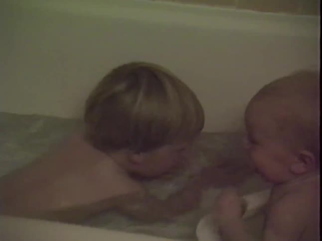 Two young children play together in a bathtub during a cozy home bath time