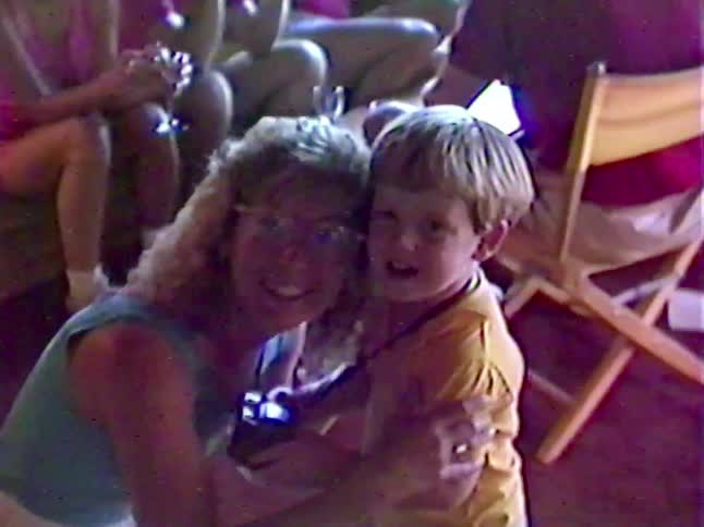 A sweet vintage home video shows a mother playfully putting her glasses on her young son as they pose together with an old camera