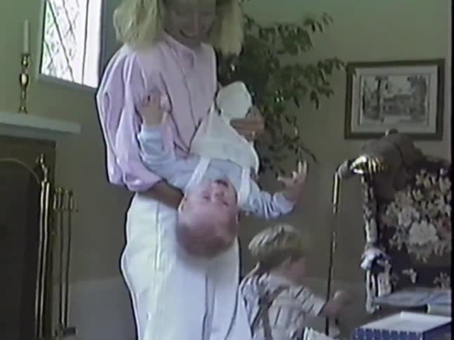 A mother playfully lifts her baby into the air and holds him upside down in their living room in this nostalgic home video footage