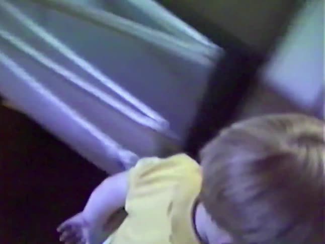 A little boy in a yellow shirt learns to play catch with his dad in the living room in this heartwarming vintage home video