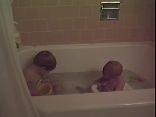 Two young children sit and play together during bath time in a home bathtub