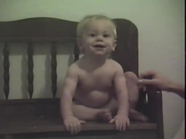 Vintage home video footage shows a cute baby in a diaper laughing hysterically while sitting on a wooden bench