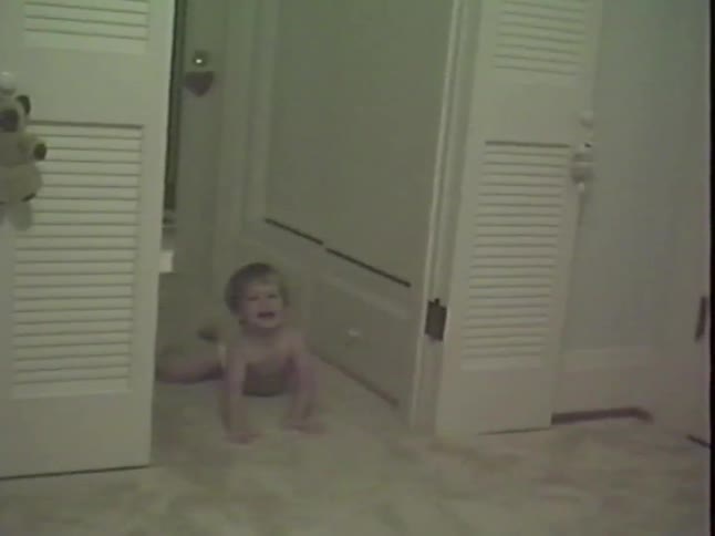 Vintage VHS footage shows a smiling baby crawling down a hallway in a home