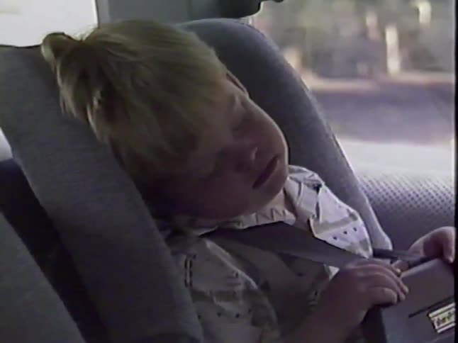 A vintage home video shows a cute toddler sleeping soundly in his car seat during a family road trip