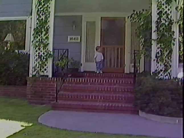 A mother with her toddler and baby emerges from her suburban home to pose for a heartwarming family portrait on the front porch in this vintage home video