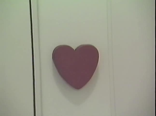 A slow zoom into a pink heart-shaped knob on a white closet door from the 1980s