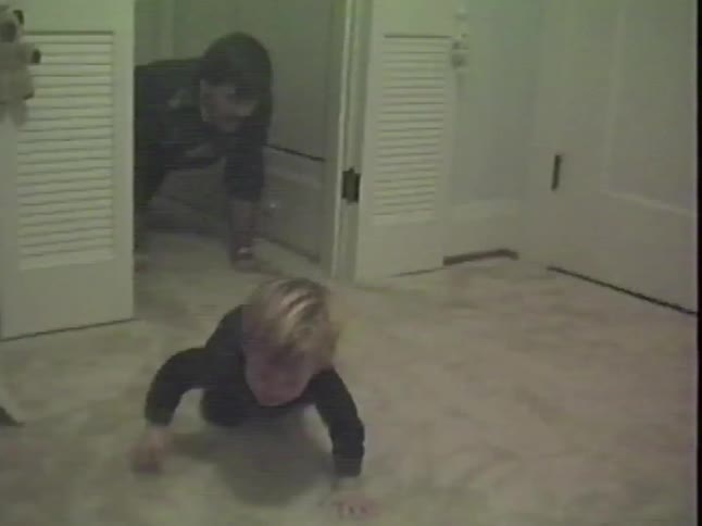 Vintage home video captures a funny moment as a father and his two young sons crawl together on the carpet