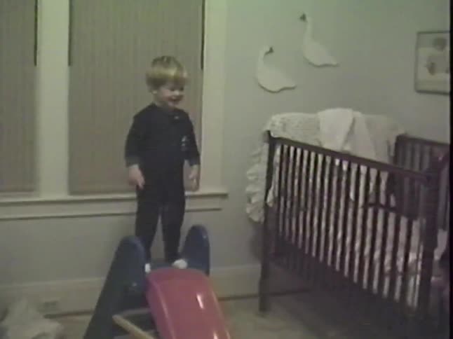 A happy toddler in pajamas excitedly climbs and slides down his indoor toy slide as his father watches