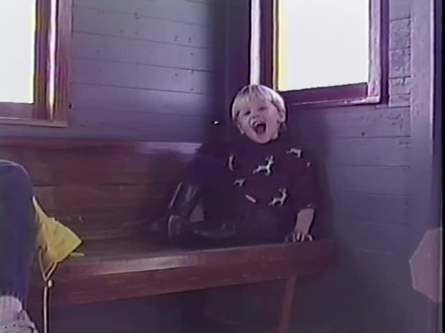 Vintage home video footage of a cute little boy laughing happily while sitting on a wooden bench