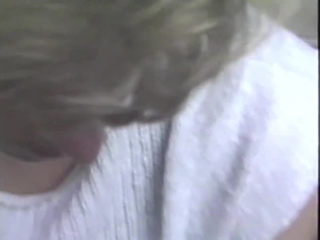 A woman with short blonde hair reads a newspaper while sitting on her porch steps in this vintage 1980s footage