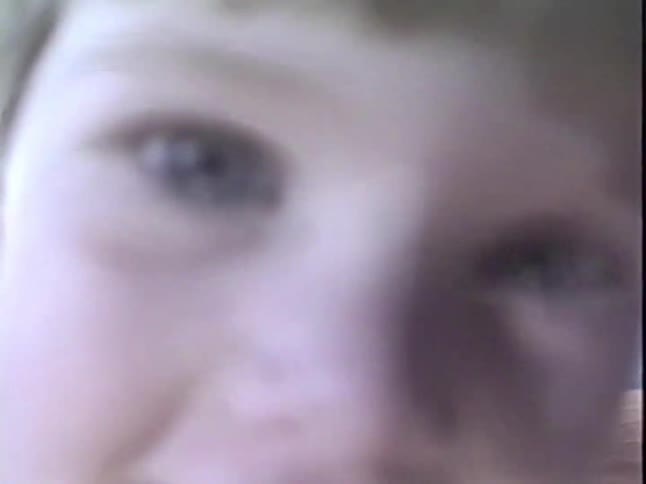 An adorable little boy in a winter sweater smiles and laughs while getting close to the camera in this vintage home video