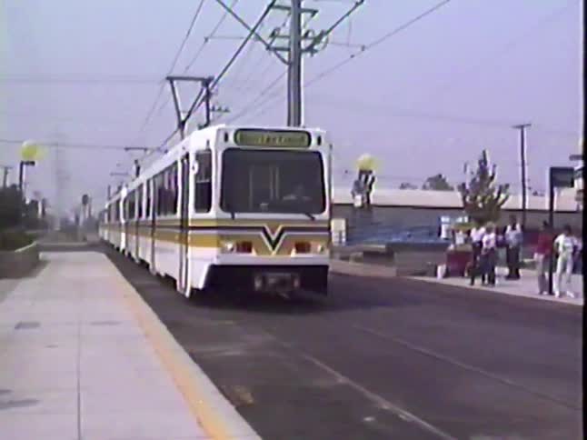A vintage light rail train with yellow and blue stripes arrives at an outdoor station in this archival home movie footage