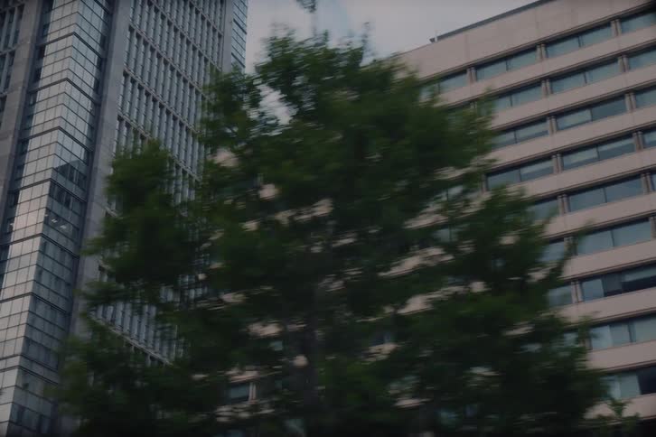Passing by towering city skyscrapers and lush green trees in a slow-motion tracking shot