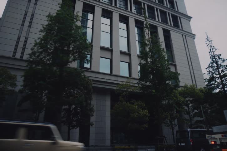 A cinematic low-angle view of traffic moving past a modern office building on a city street