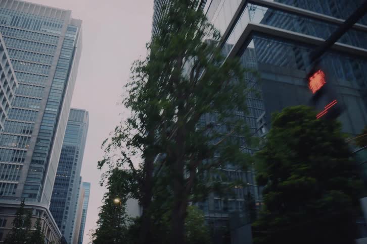 Looking up at towering modern skyscrapers and office buildings while driving through a metropolitan business district on a cloudy day