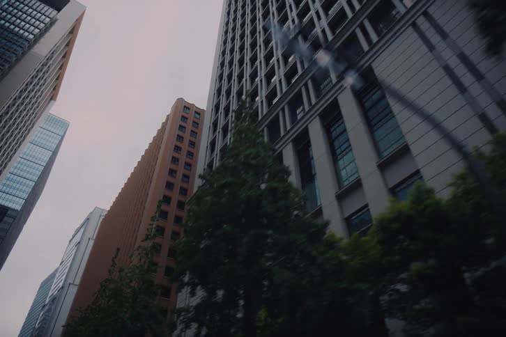 A smooth, low-angle tracking shot reveals the towering architecture of city skyscrapers against an overcast sky