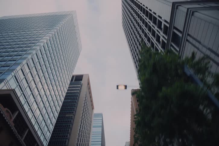 A slow moving, low-angle pull-back shot reveals the towering modern skyscrapers of a financial district under an overcast sky