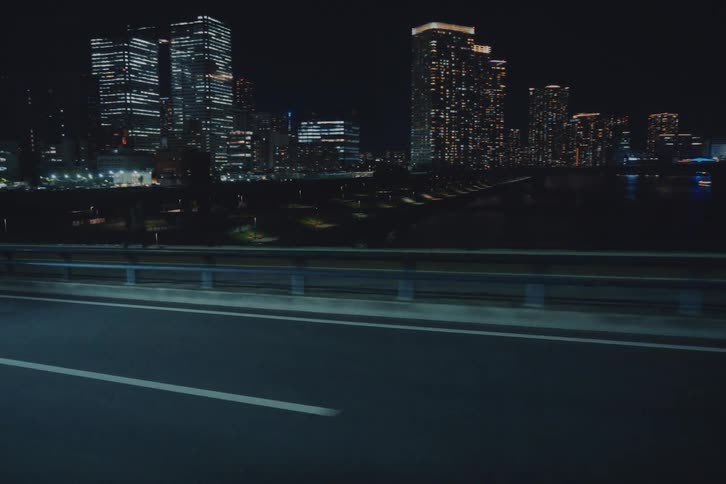 Side view from a moving vehicle on a highway, showcasing a vibrant city skyline illuminated against the dark night sky