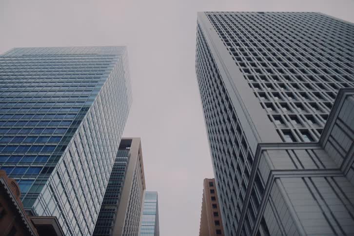A slow dolly shot reveals the towering modern skyscrapers of a city's financial district under an overcast sky