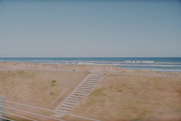 A nostalgic point-of-view shot from a moving vehicle driving along a coastal highway overlooking the ocean on a sunny day