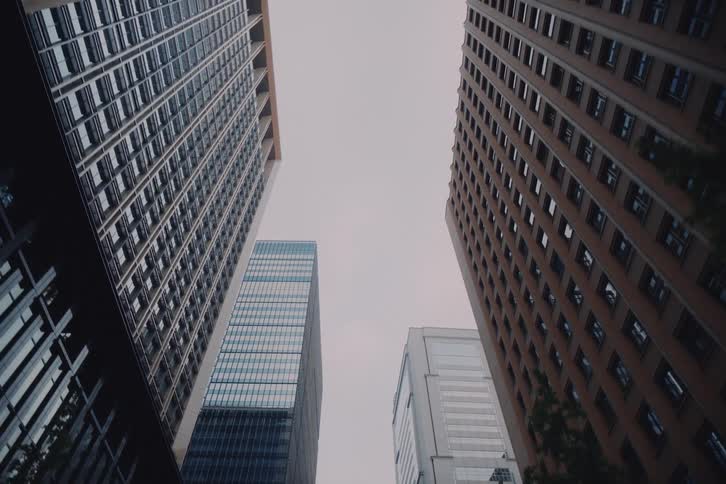 A cinematic low-angle shot slowly pulls back and tilts up to reveal towering skyscrapers against an overcast sky