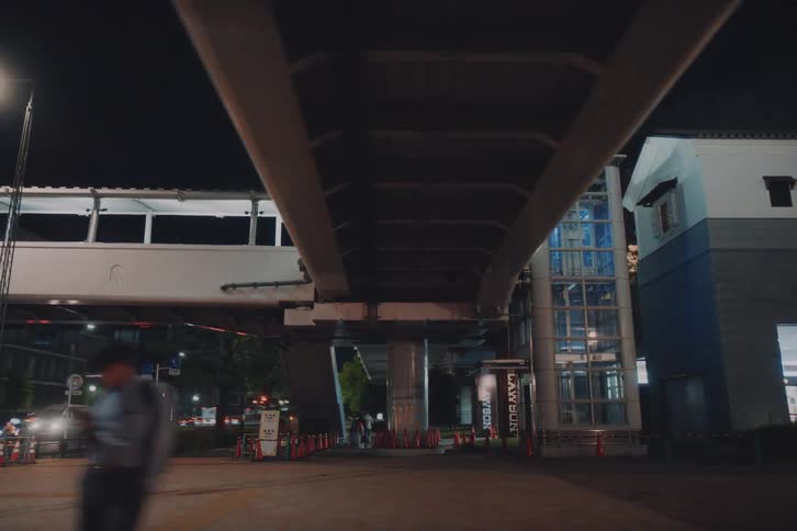 Smooth point-of-view shot driving past a modern illuminated pedestrian overpass in Tokyo at night